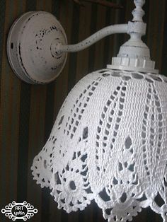 an old fashioned white lamp hanging from a wall with lace on the shade and cord