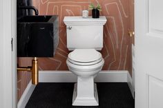 a white toilet sitting inside of a bathroom next to a black and gold trash can