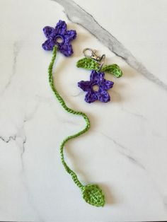 two crocheted flowers on a white marble counter with green stems attached to them