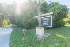 a sign that is in the grass near some bushes and trees with sun shining on it