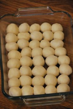 several balls of dough in a glass dish on a wooden counter top, ready to be cooked