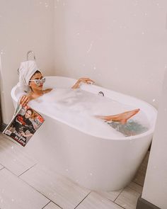 a woman laying in a bathtub with magazine next to her