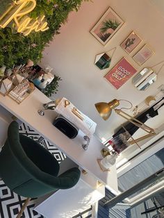 a room with plants and pictures on the wall, including a green chair next to a desk