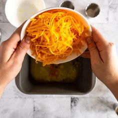 two hands holding a white bowl filled with shredded carrots