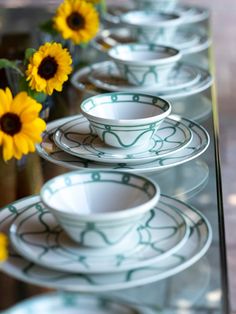 a row of white and green dishes sitting on top of a glass table next to yellow flowers