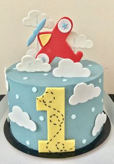 a blue cake with a red plane on top and clouds in the sky around it