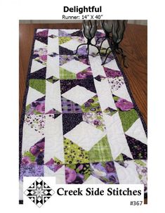 a quilted table runner with purple and green flowers on it, sitting on a wooden floor