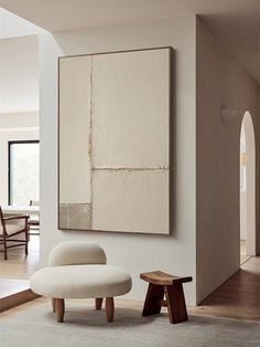 an abstract painting hangs on the wall next to a white chair and footstool