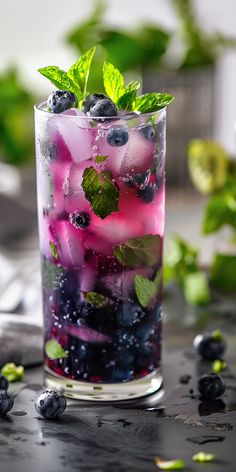 a glass filled with blueberries and mint sprits on top of a table