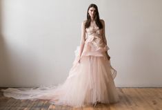 a woman in a pink dress standing on a wooden floor with her hands behind her back