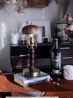 a lamp sitting on top of a wooden table next to a bottle of alcohol and flowers