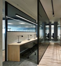 an office with glass walls and desks in the middle, along with wooden flooring