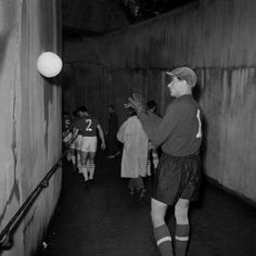 black and white photograph of men playing soccer in an alleyway with one man reaching up to catch the ball