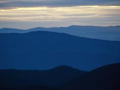 the mountains are covered in dark blue hues as the sun is setting over them