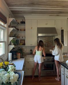 two young women standing in a kitchen with white cabinets and wood flooring, looking at an oven