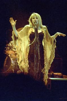 a woman standing in front of a microphone and holding her hands out to the side