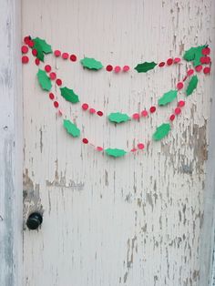 an old door decorated with red and green paper holly garlands on white paint peeling from the wall