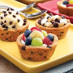 three mini desserts with fruit and chocolate chips on a yellow tray next to silverware