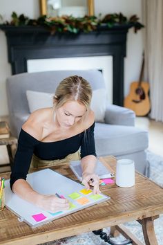 a woman sitting at a table working on some art work with markers and pencils