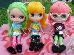 three dolls sitting on top of a pink blanket in the grass next to each other