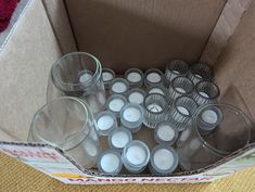 a cardboard box filled with lots of clear cups and votive candles on top of a table