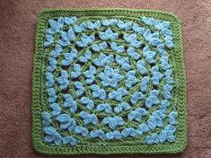 a crocheted square with blue flowers on it sitting on the floor next to a carpet