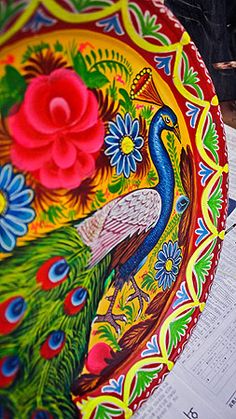 a colorful peacock plate sitting on top of a table next to an open book and pen