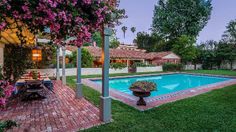 an outdoor swimming pool surrounded by lush green grass and pink flowers in front of a house