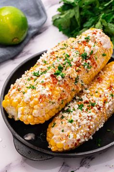 two corn on the cob with parsley and cilantro in a cast iron skillet