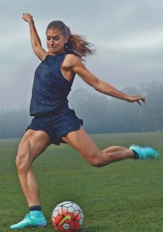 a woman kicking a soccer ball on top of a field