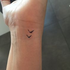 a small tattoo on the wrist of a woman with two birds flying over her head