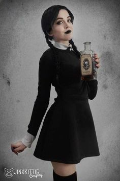 a woman dressed in black holding a bottle and looking at the camera with an evil look on her face