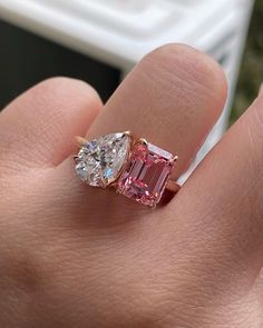 a woman's hand holding an engagement ring with two pink and white diamonds on it