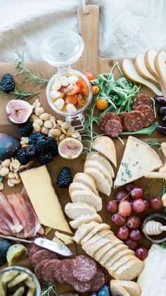 an assortment of cheeses, meats and fruit on a cutting board with wine glasses