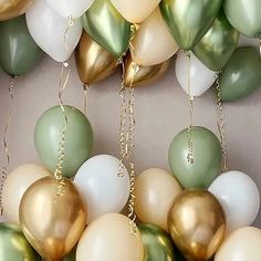 many balloons are hanging from the ceiling with gold and green accents on them, as well as white and gray ones