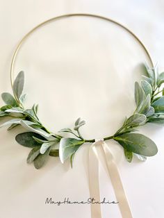 a circular wreath with green leaves and ribbon tied around the edges on a white background