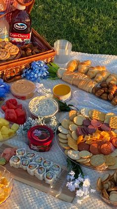 an assortment of food is laid out on a picnic blanket in front of the grass