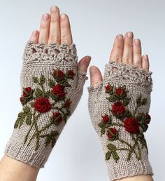 a woman's hand is holding up a knitted glove with flowers on it