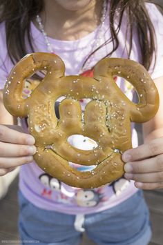 a girl holding up a mickey mouse pretzel