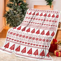 a red and white blanket with christmas trees on it sitting in front of a fireplace