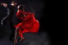 two people dressed in black and red are dancing on a dark background with their arms spread out