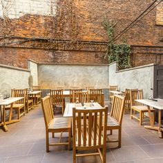 an outdoor dining area with wooden tables and chairs, against a brick wall that has vines growing on it