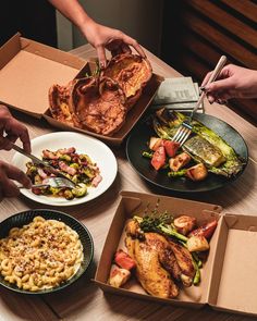 people are eating food out of boxes on a table with utensils and plates