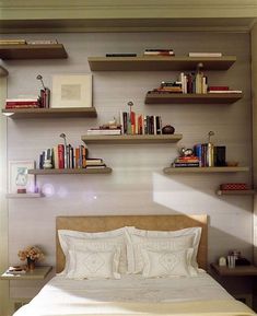 there is a bed with white sheets and books on the shelves above it in this bedroom