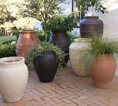 several large vases are lined up on the brick walkway in front of a house