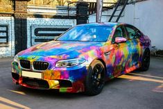 a colorful bmw car parked in front of a white brick building with graffiti on it