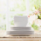 a stack of white plates sitting on top of a wooden table next to a vase with flowers