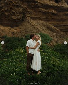 a man and woman standing next to each other on a lush green field with rocks in the background