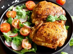 two pieces of chicken on a plate with tomatoes, lettuce and tomato slices