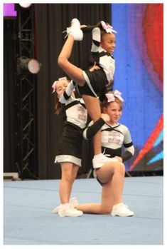 two cheerleaders performing on the stage with their arms in the air and one holding her leg up